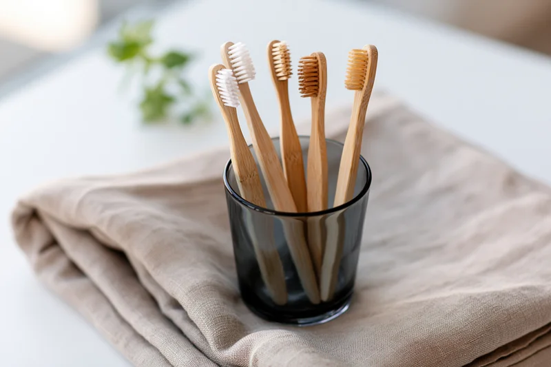 Bamboo toothbrushes with mixed bristle colors standing in a glass cup on a folded linen towel