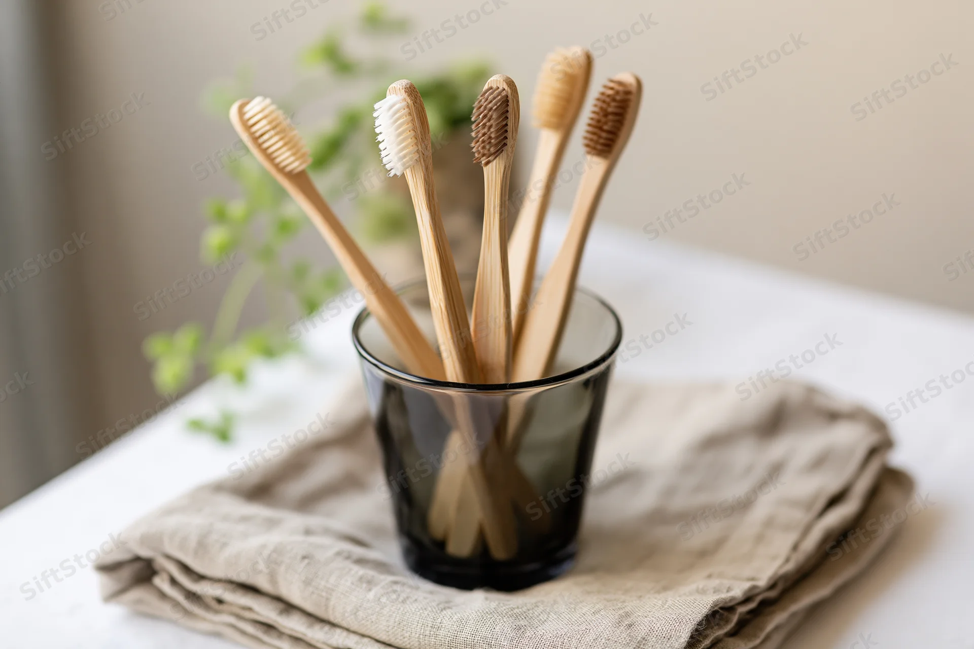 Bamboo toothbrushes with mixed bristle colors standing in a glass cup on a folded linen towel on a bathroom countertop