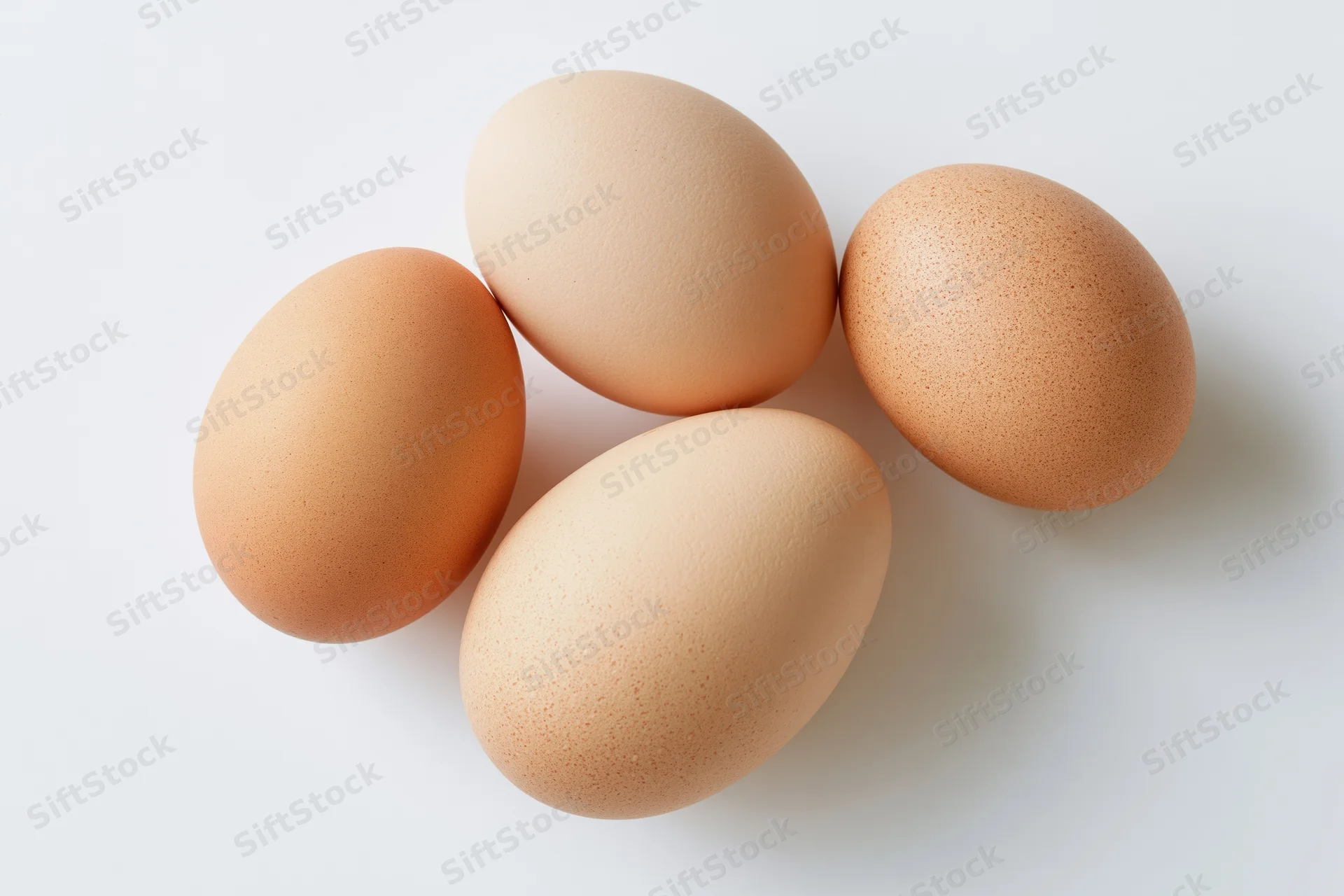 Four brown chicken eggs arranged loosely on a flat white surface