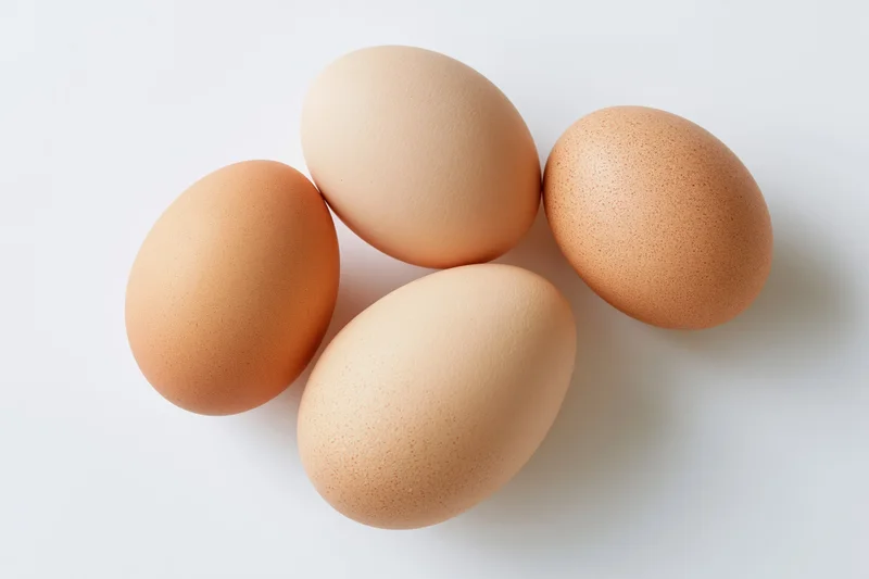 Four brown chicken eggs arranged loosely on a flat white surface