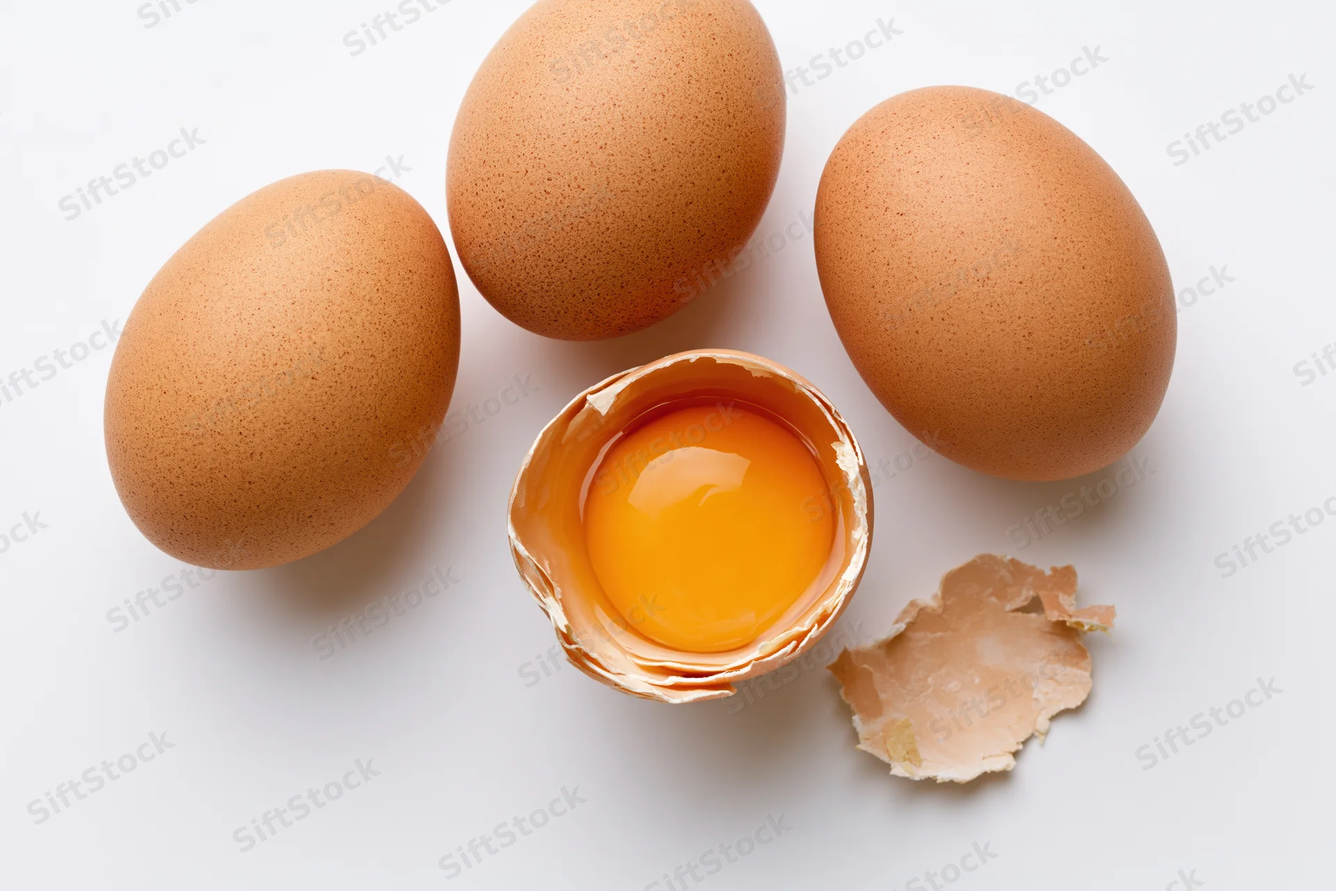 Four brown chicken eggs arranged on white surface with one cracked open showing yolk and shell fragments
