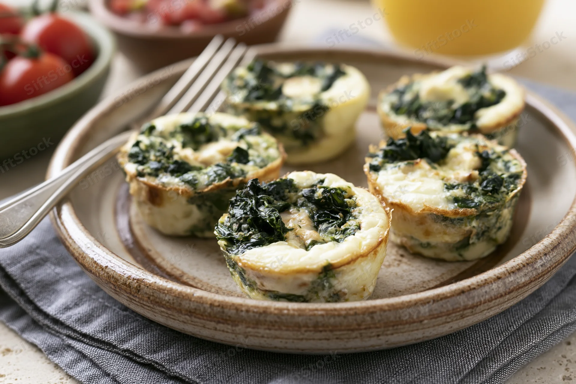 Four egg muffin cups with spinach and chicken arranged on a rustic ceramic plate with a fork and napkin on a table