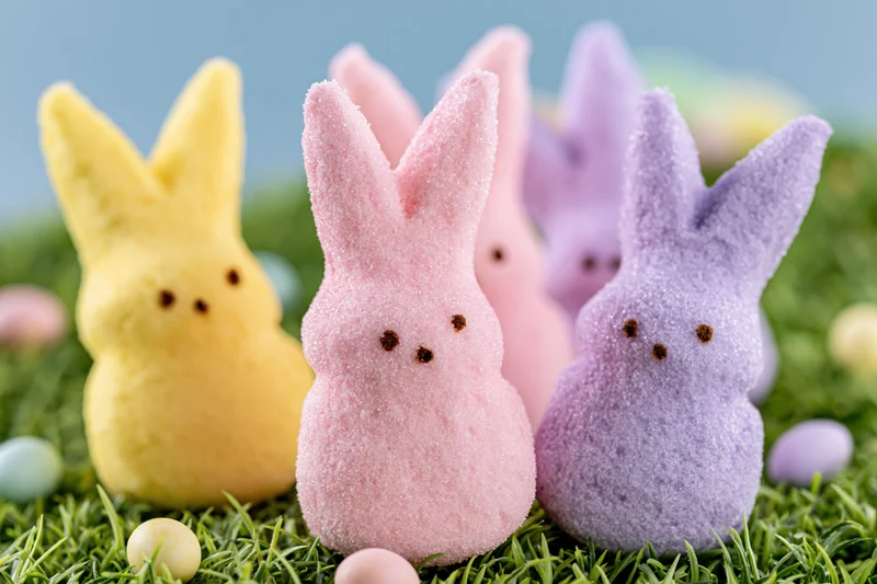 Marshmallow Peeps bunny candies in yellow, pink, and purple arranged on green grass with small eggs scattered around