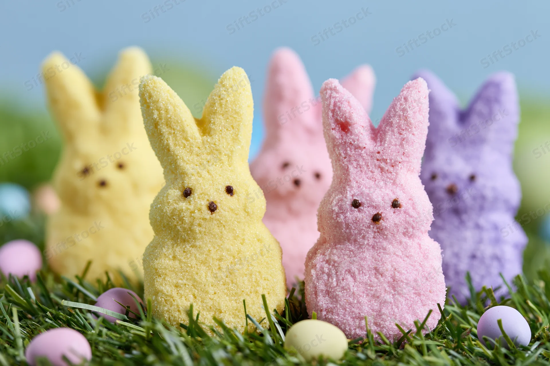 Marshmallow peeps bunny candies arranged in grass with pastel eggs for easter celebration