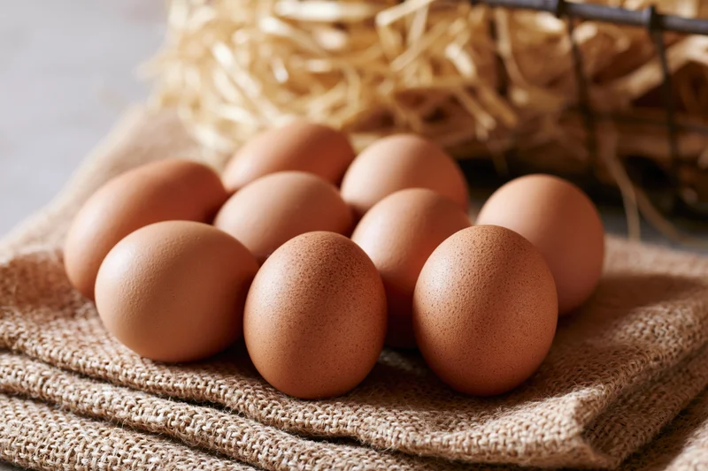 Brown chicken eggs scattered on folded burlap cloth with straw in background