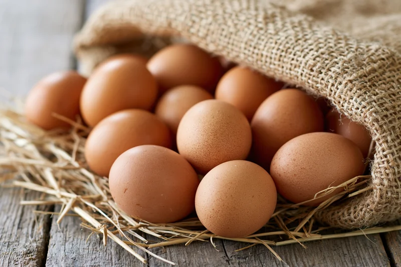 Brown chicken eggs spilling from an open burlap sack onto straw on a wooden surface