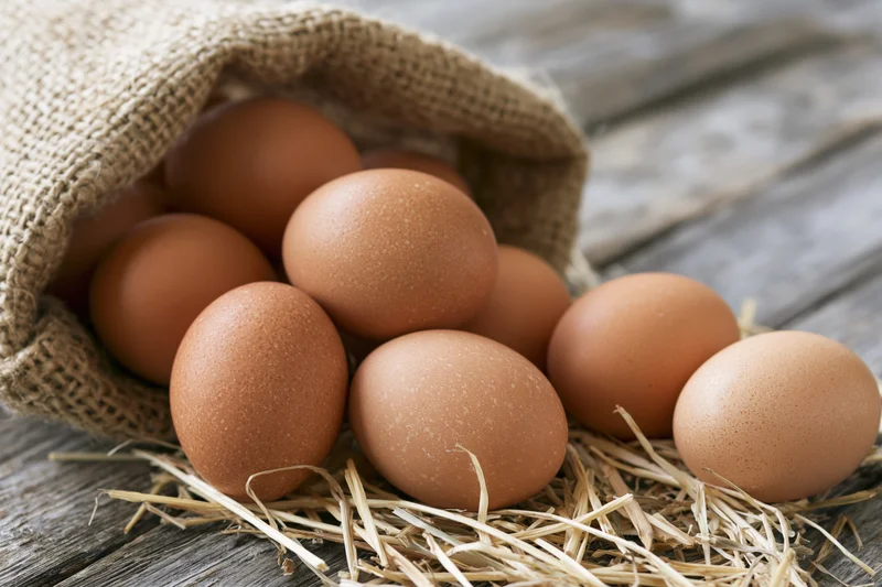 Brown chicken eggs spilling from an open burlap sack onto straw on a wooden surface