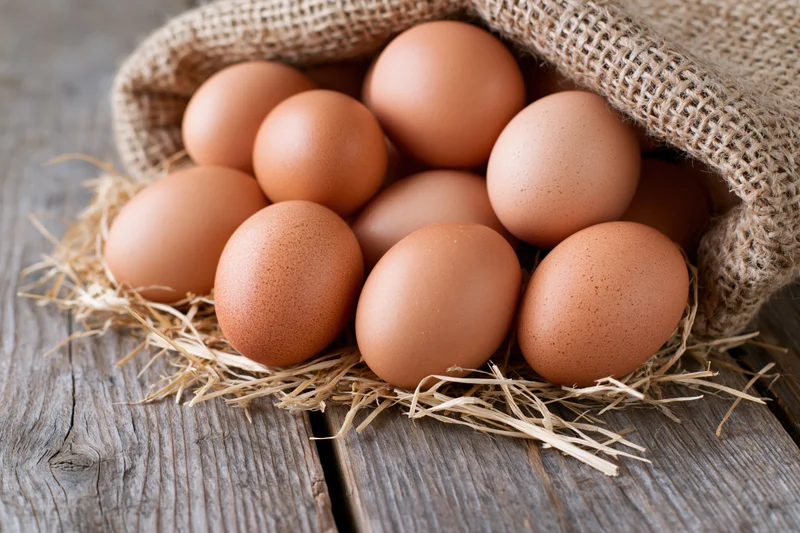 Fresh brown chicken eggs spilling from an open burlap sack onto straw on a wooden table