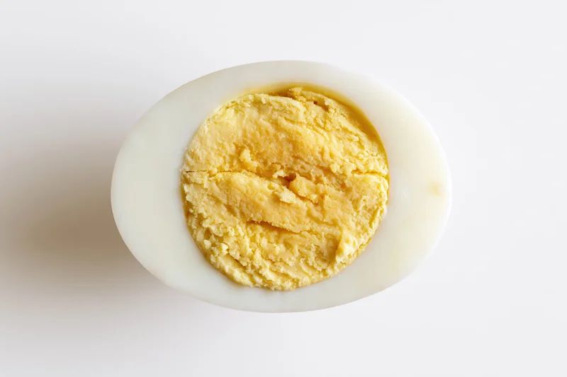 Half of a hard-boiled egg sliced lengthwise showing fully cooked yolk on white background