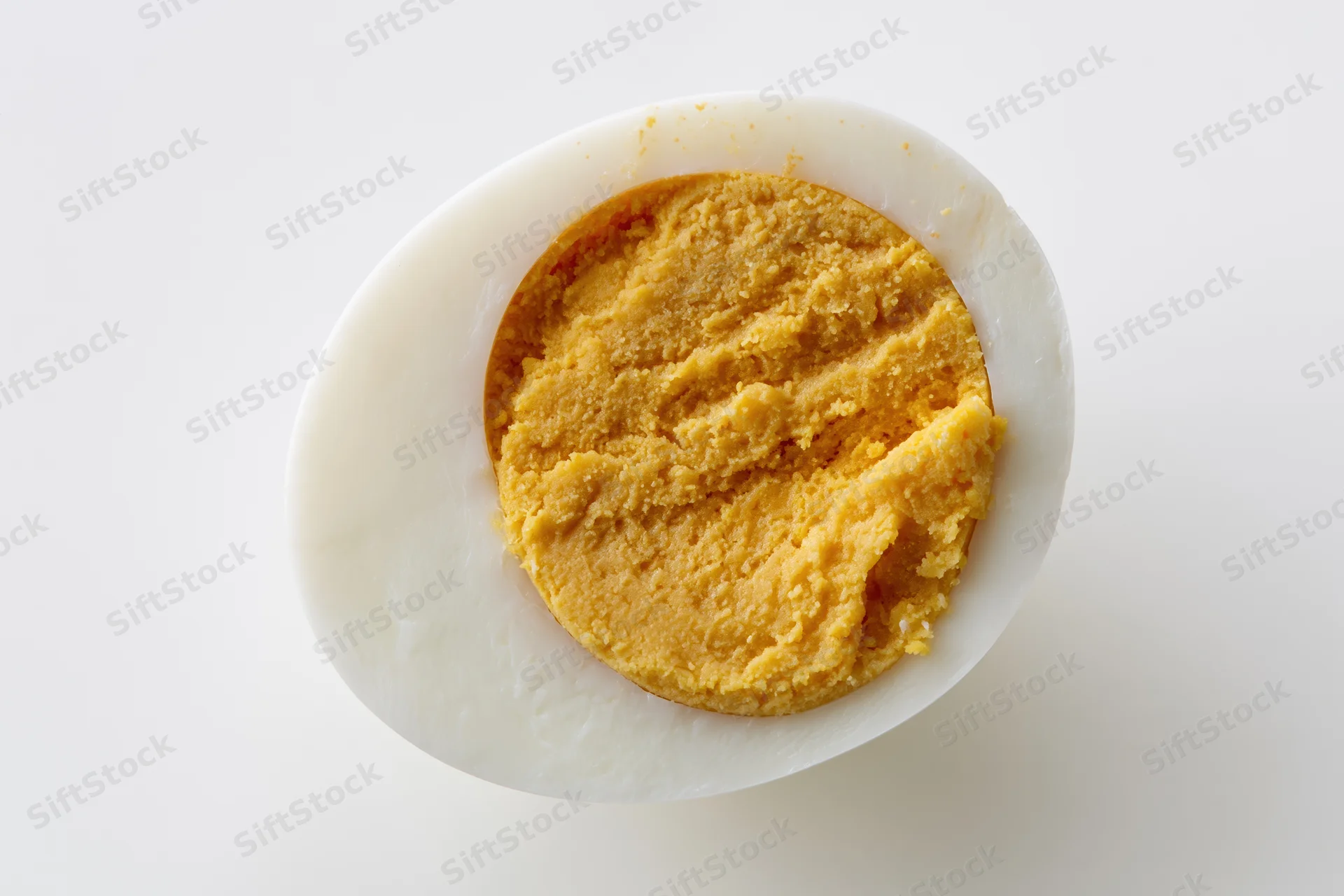 Half of a hard-boiled egg sliced lengthwise showing fully cooked yolk on white background