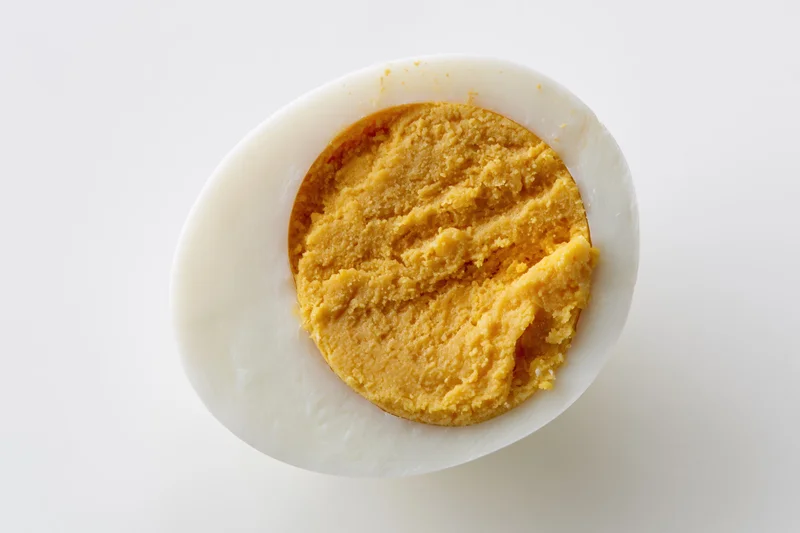 Half of a hard-boiled egg sliced lengthwise showing fully cooked yolk on white background