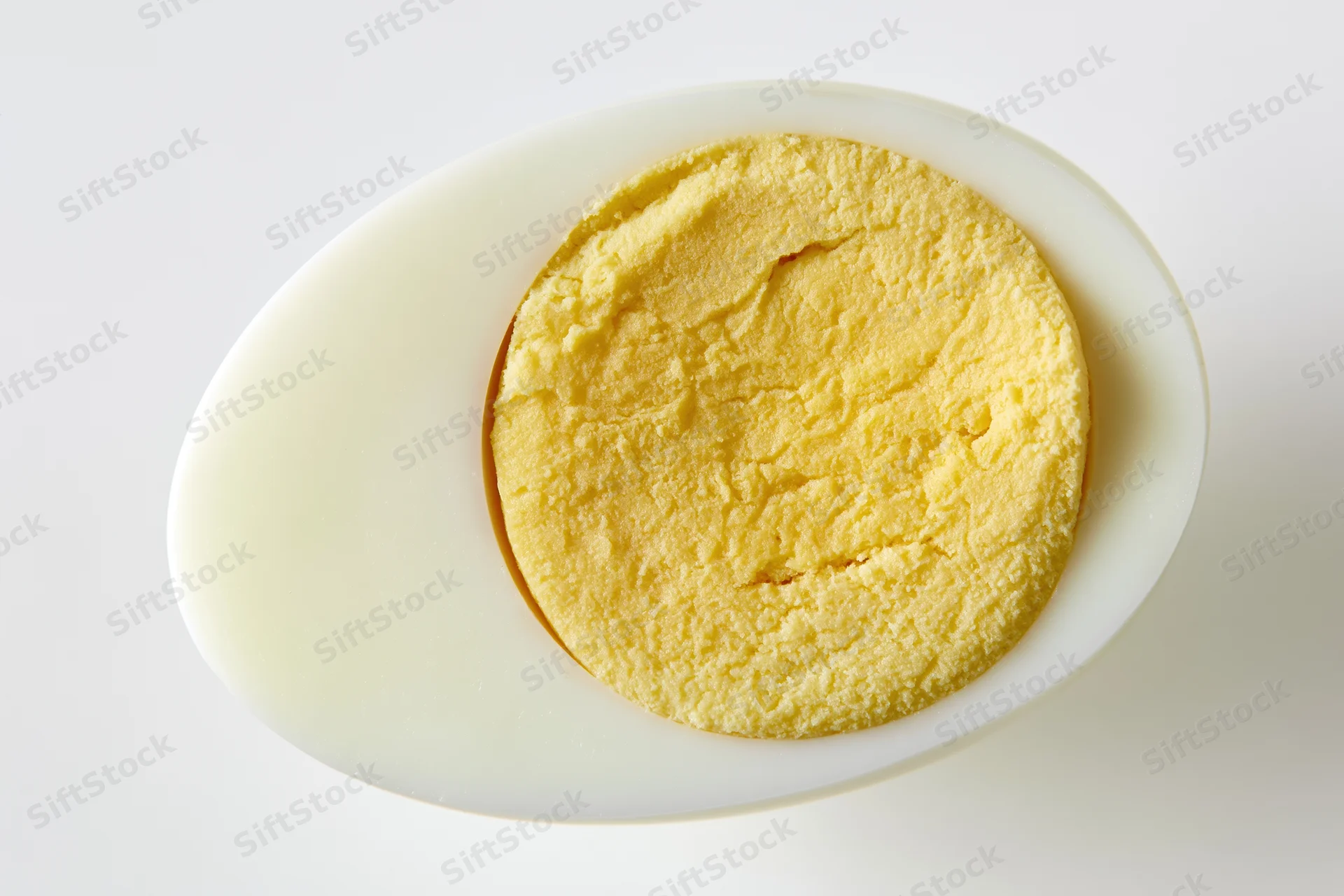 Half of a hard-boiled egg sliced lengthwise showing fully cooked yolk on white background