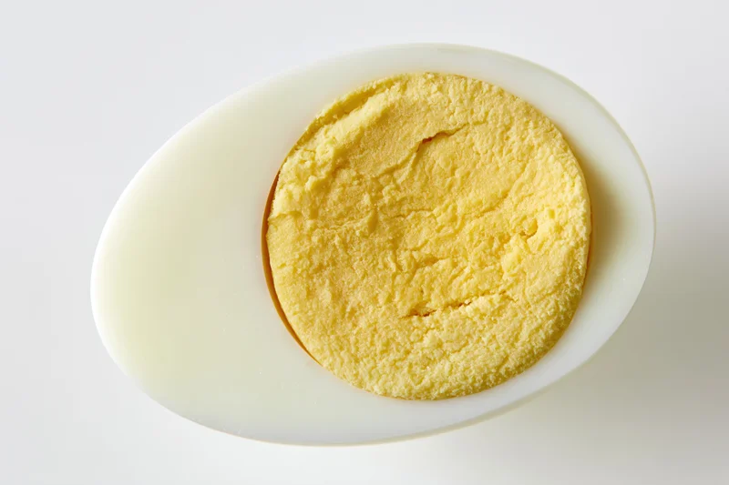 Half of a hard-boiled egg sliced lengthwise showing fully cooked yolk on white background