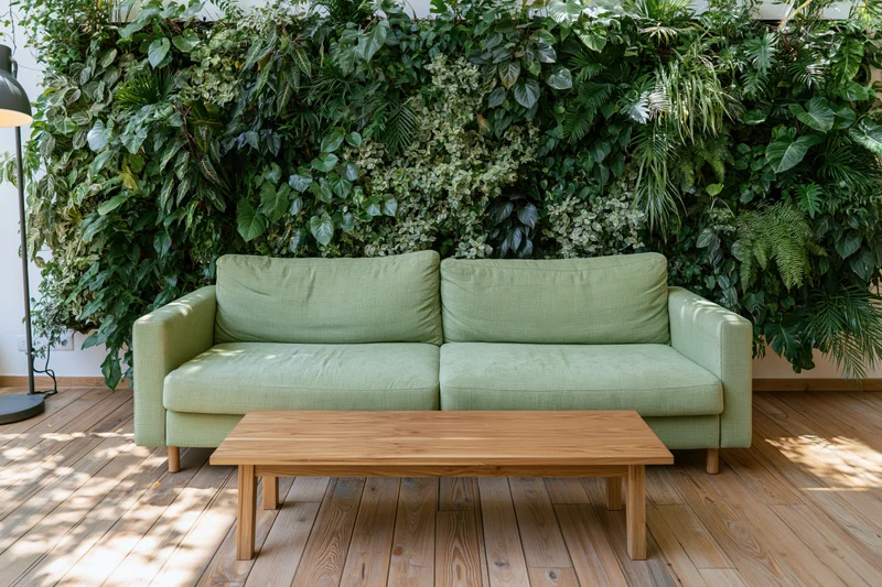 Sage green sofa with wooden coffee table in front of lush green living wall in living room