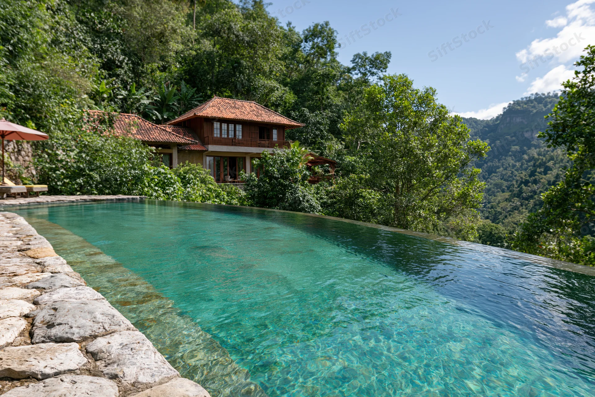 Infinity pool with clear turquoise water and natural stone edge overlooking jungle and mountains