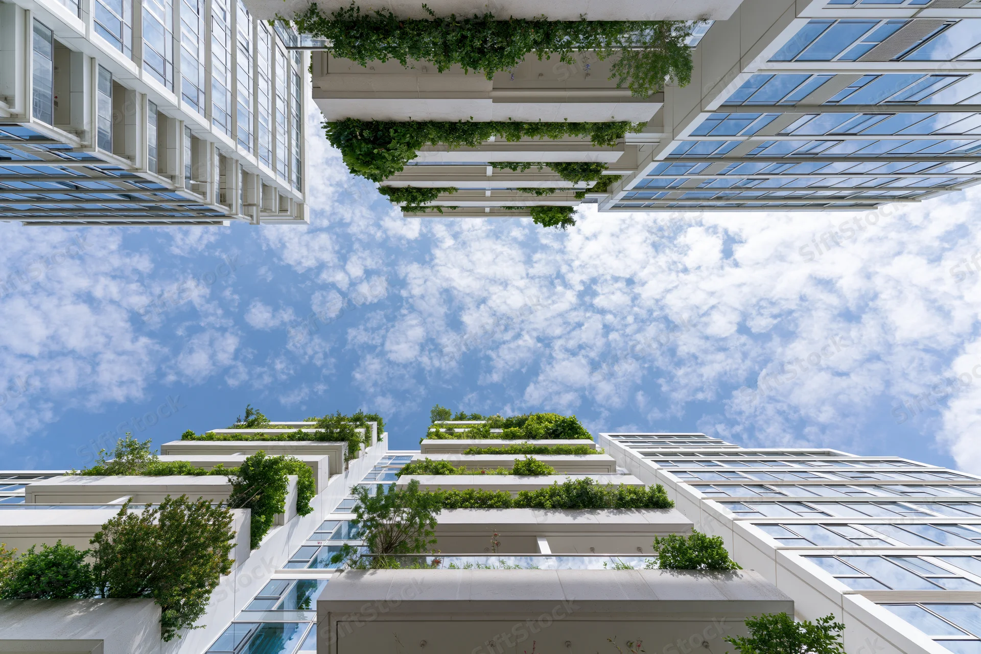Modern skyscrapers with green vertical gardens viewed from below against a blue sky