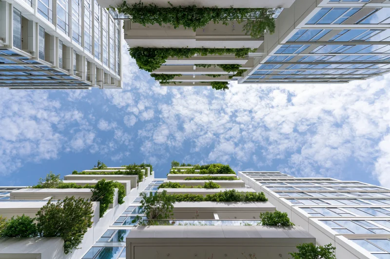 Modern skyscrapers with green vertical gardens viewed from below against a blue sky