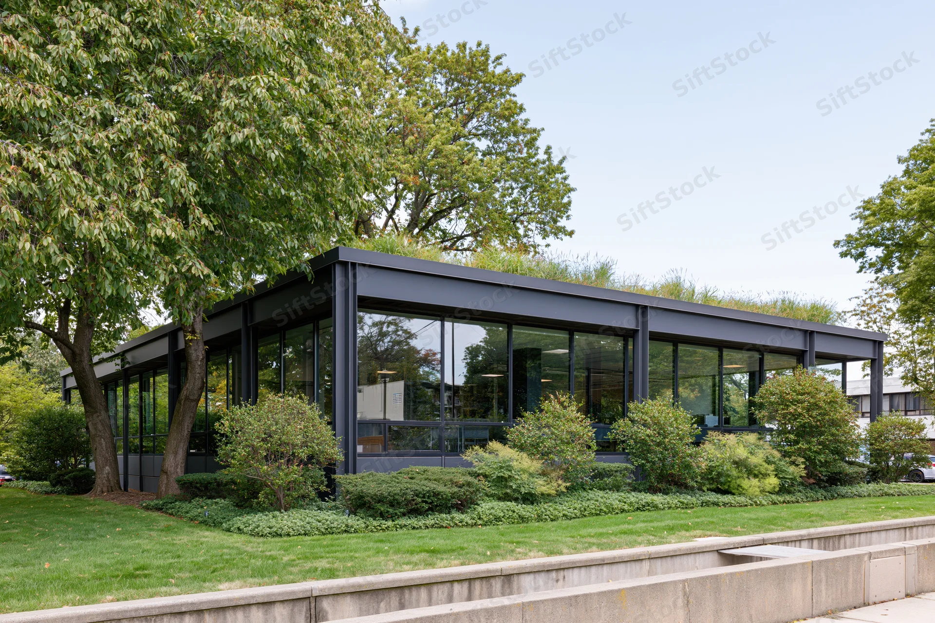 Low-rise modernist office building with dark steel frame and glass facade surrounded by trees and landscaping