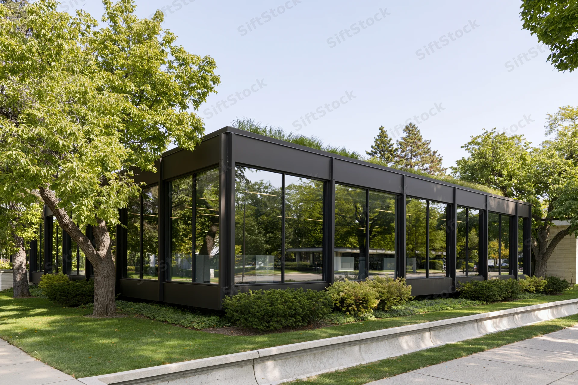 Low-rise modernist office building with dark steel frame and glass facade surrounded by trees and greenery on a sunny day