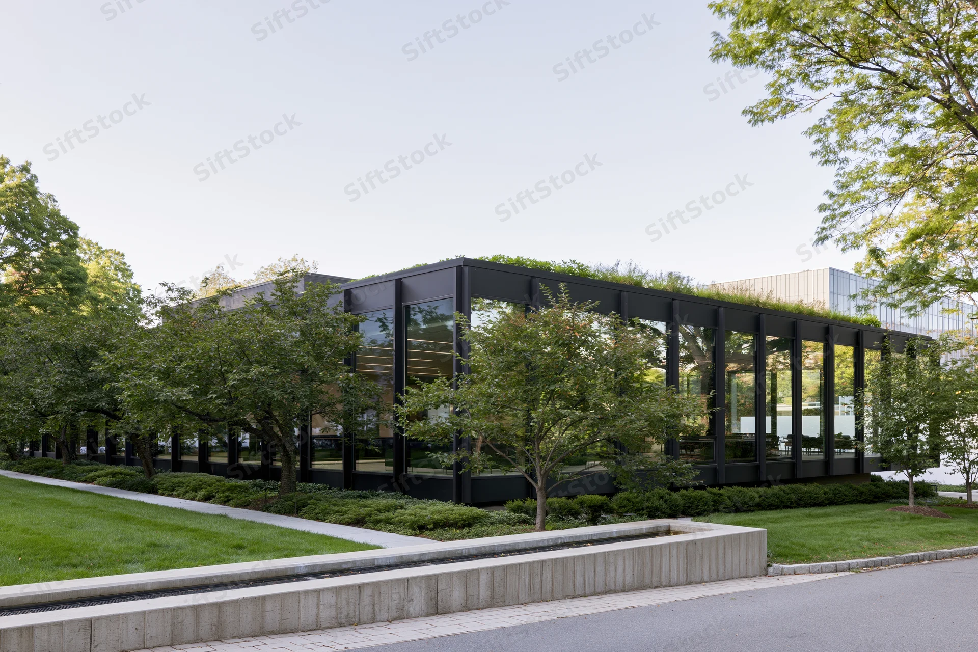 Low-rise modernist office building with dark steel frame and glass facade surrounded by landscaped greenery and trees