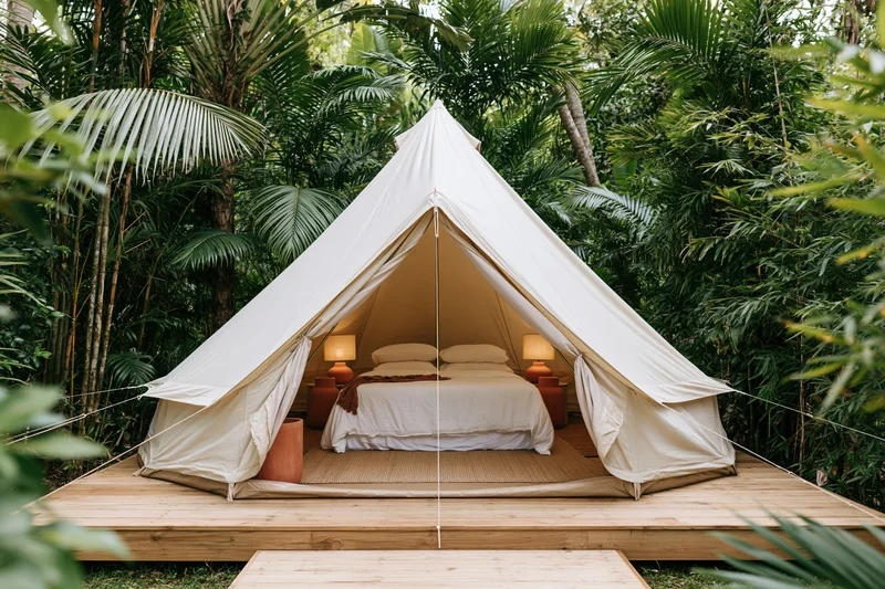 Luxury bell tent with open canvas flaps revealing a bed on a wooden deck surrounded by tropical foliage