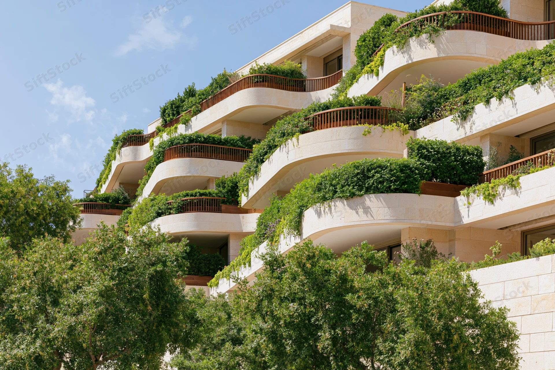 Luxury residential apartment complex with curved wraparound balconies covered in greenery under a blue sky