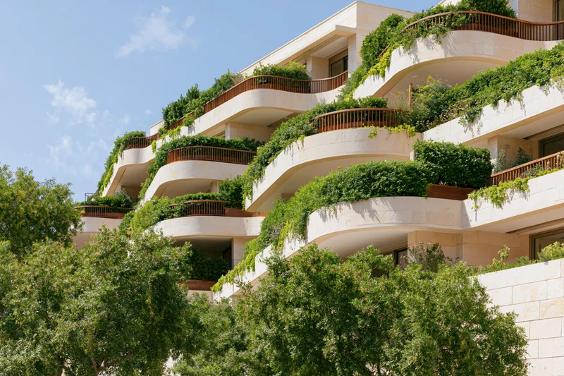 Luxury residential apartment complex with curved wraparound balconies covered in greenery under a blue sky