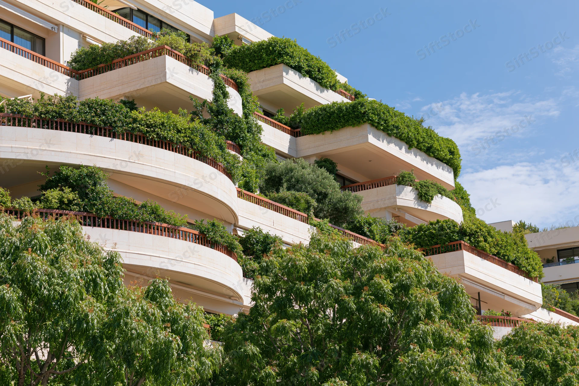 Luxury residential apartment complex with curved wraparound balconies covered in greenery under a clear blue sky