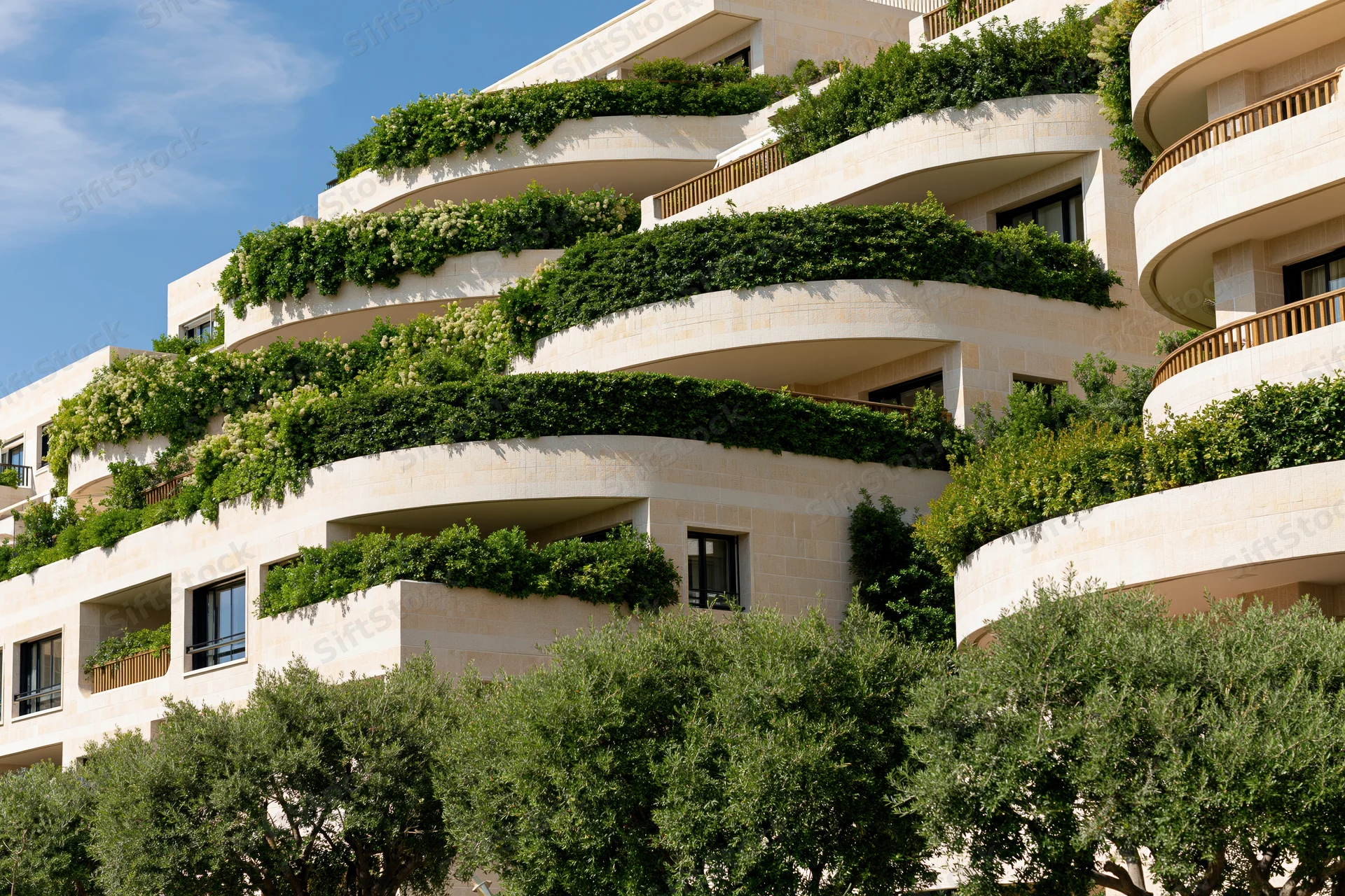 Luxury residential apartment complex with curved wraparound balconies covered in greenery under a clear blue sky