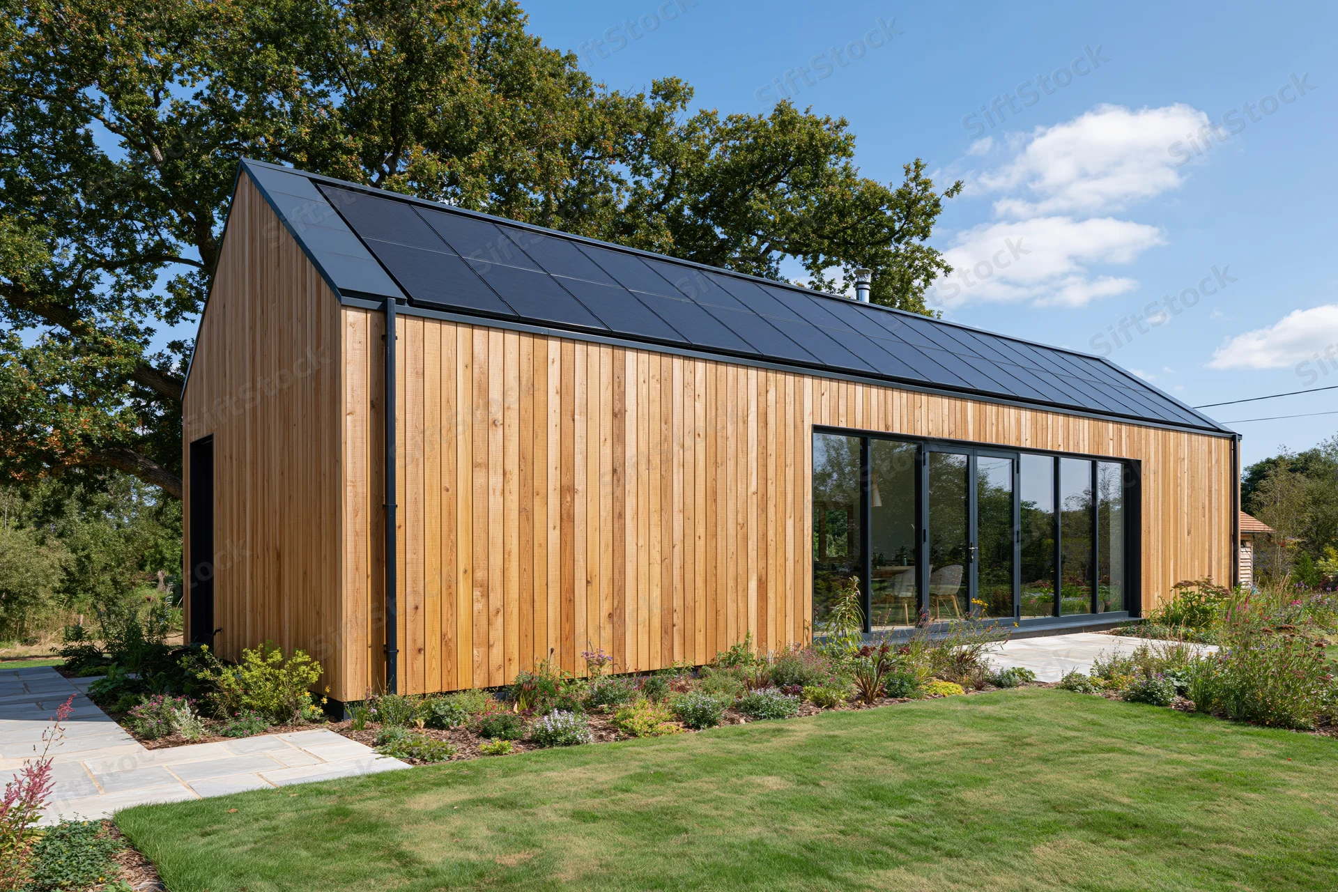 Modern barn-style house with vertical timber cladding and solar panels on roof surrounded by garden and lawn