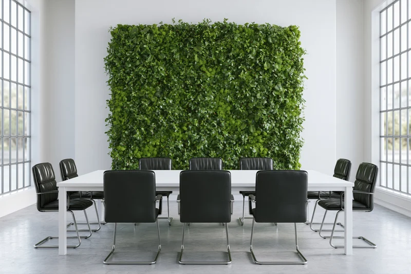 Modern conference room with white table and black chairs arranged around a green living wall in a bright office space