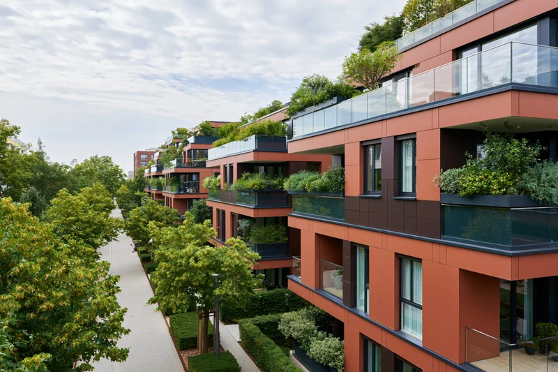 Modern residential apartment complex with rooftop gardens and balconies lined with greenery along a tree-lined pathway