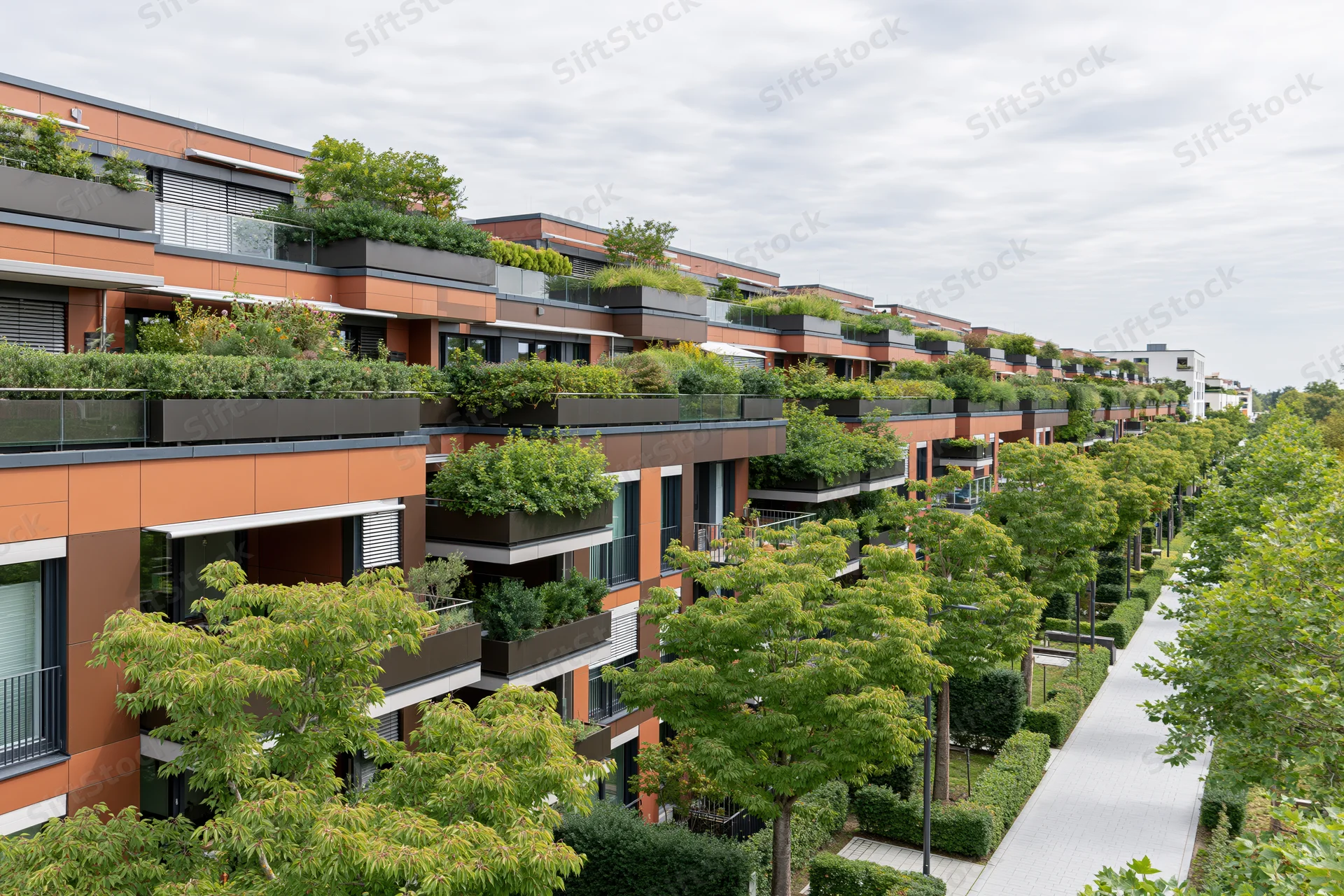 Modern apartment complex with rooftop gardens and tree-lined pathway along the exterior facade