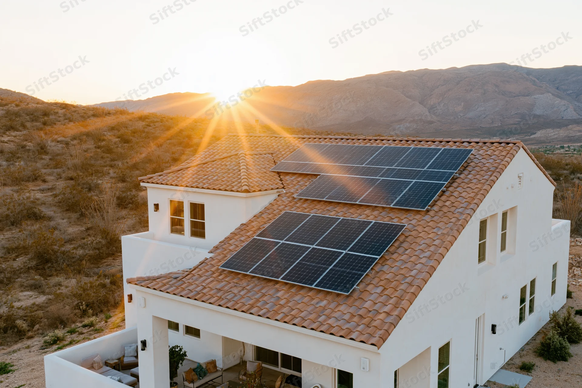 Modern white stucco house with solar panels on tiled roof in desert landscape at sunset