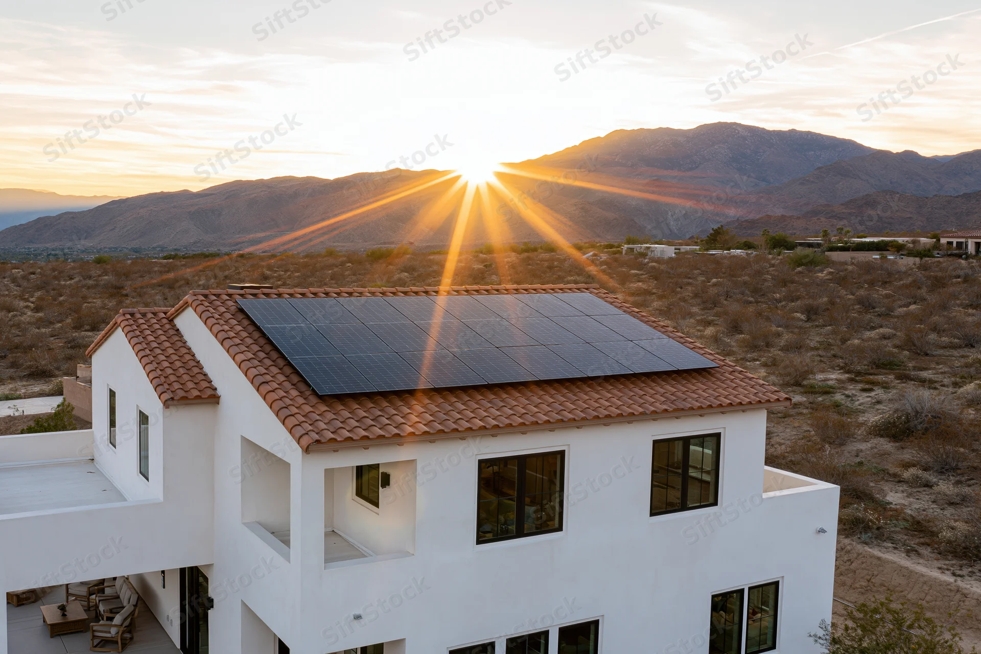 Modern white stucco house with solar panels on roof in desert at sunset