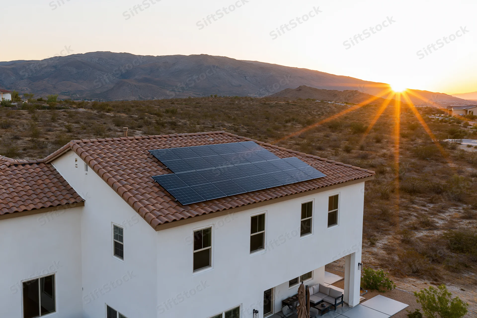 Modern white stucco house with solar panels on terracotta roof in desert landscape at sunset