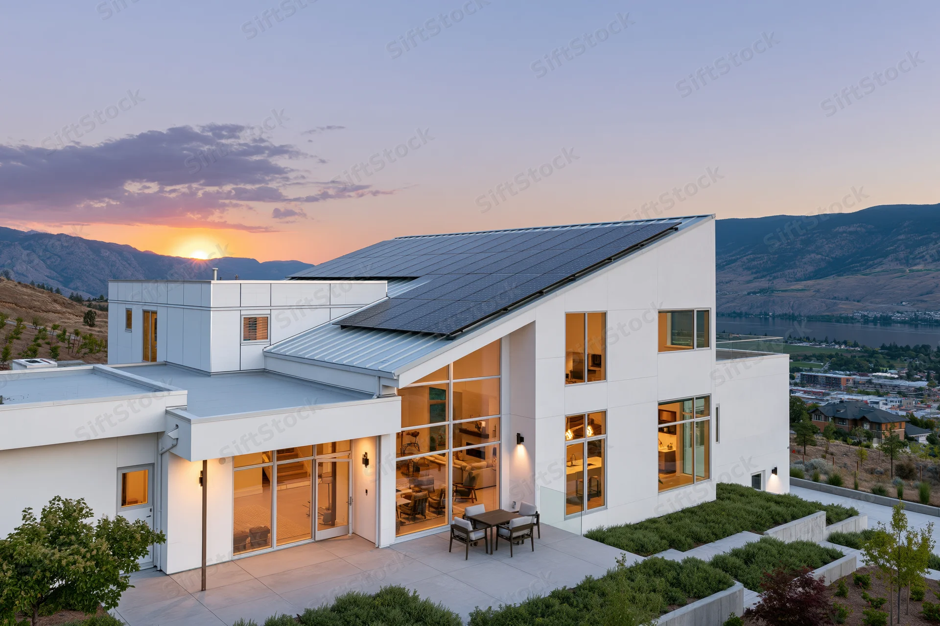 Modern white stucco house with solar panels on angled roof at sunset overlooking mountains and valley
