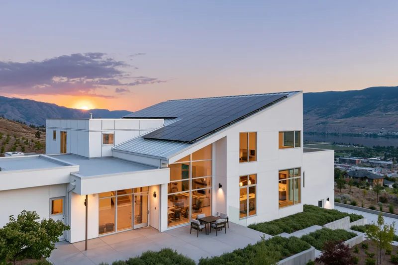 Modern white stucco house with solar panels on angled roof at sunset overlooking mountains and valley