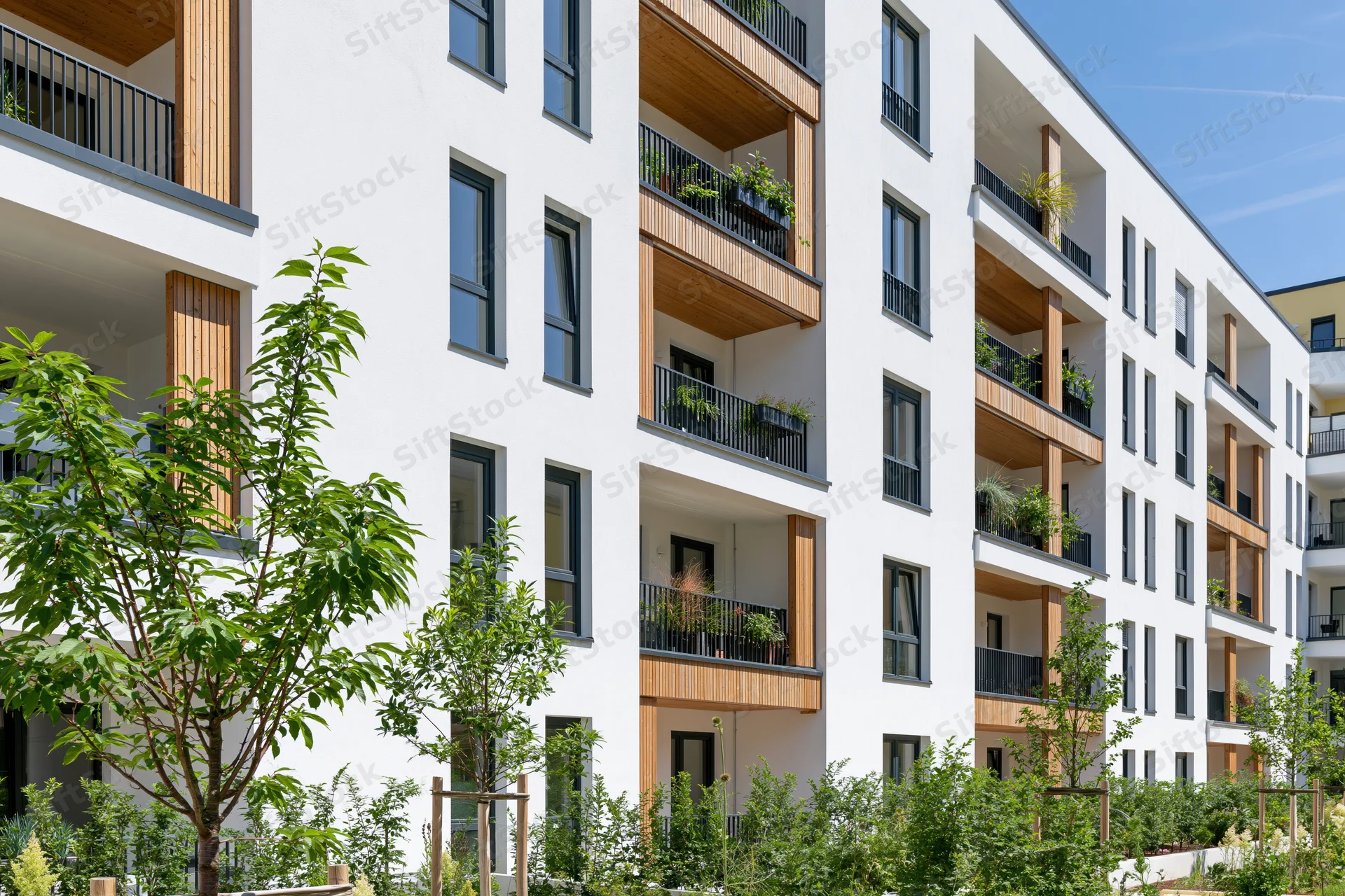 Modern white residential apartment building with wooden balconies and green landscaping in urban courtyard setting
