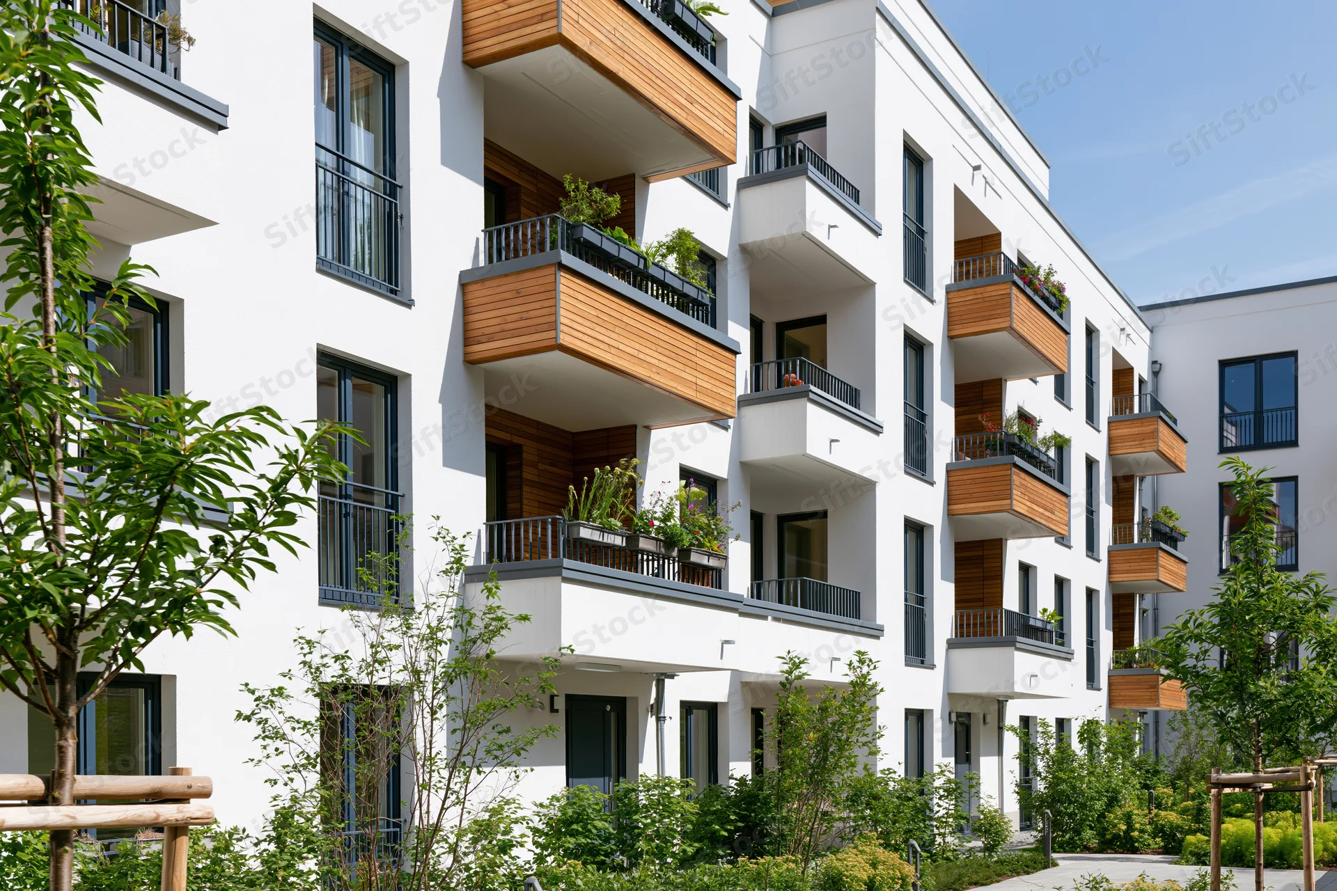 Modern white residential apartment building with wooden balconies and green landscaping in a courtyard setting
