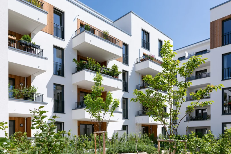 Modern white residential apartment building with wooden balconies and green landscaping in a courtyard setting