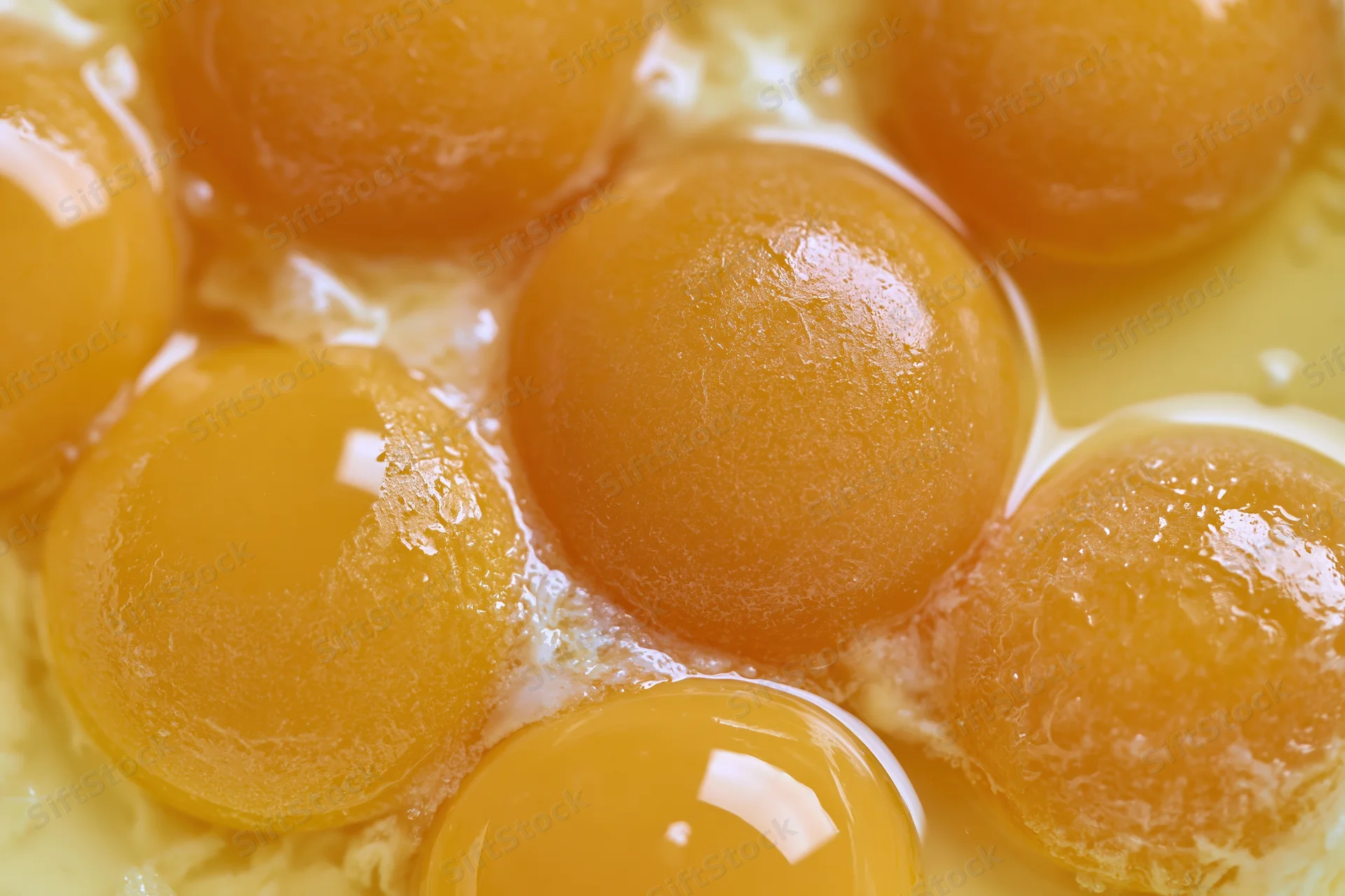 Multiple raw egg yolks cracked into a bowl viewed from directly above