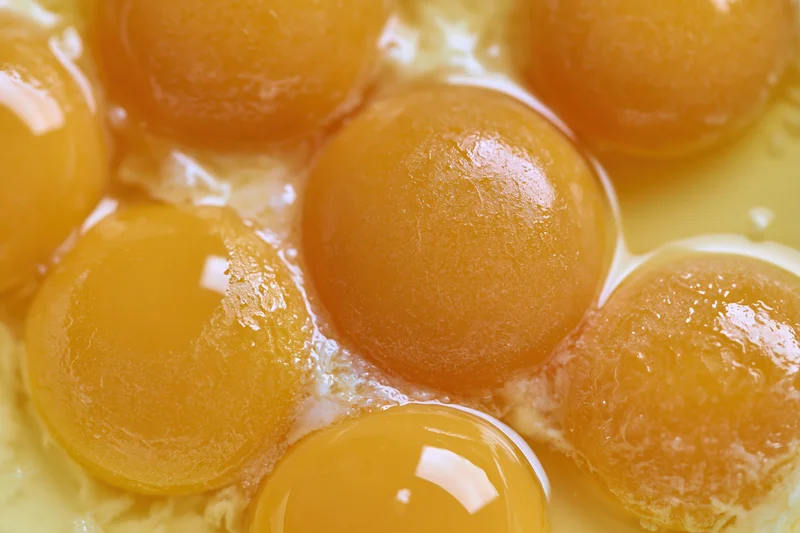 Multiple raw egg yolks cracked into a bowl viewed from directly above