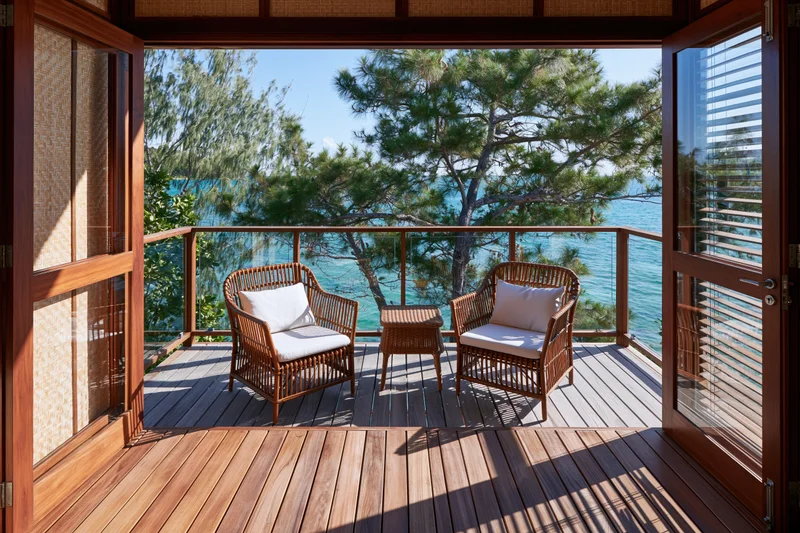 Wooden terrace with wicker furniture overlooking ocean and trees from a tropical eco-resort bungalow