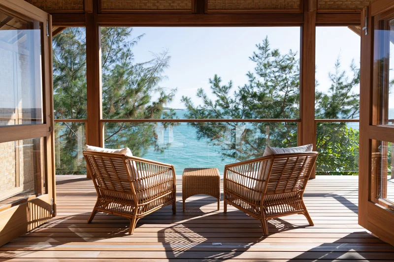 Two wicker chairs with cushions on a wooden terrace facing the