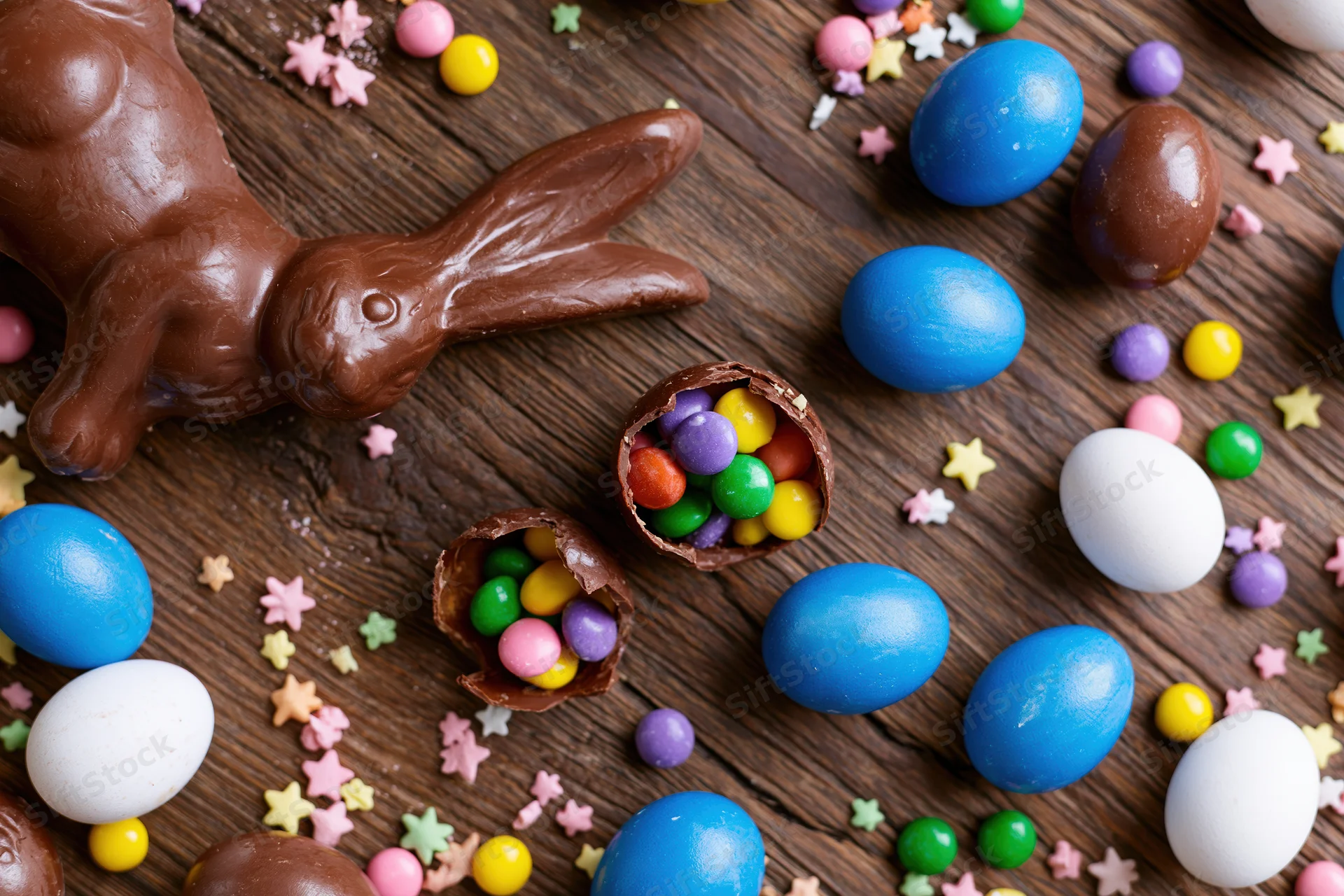 Chocolate easter bunny and colorful candy eggs arranged on dark wooden surface