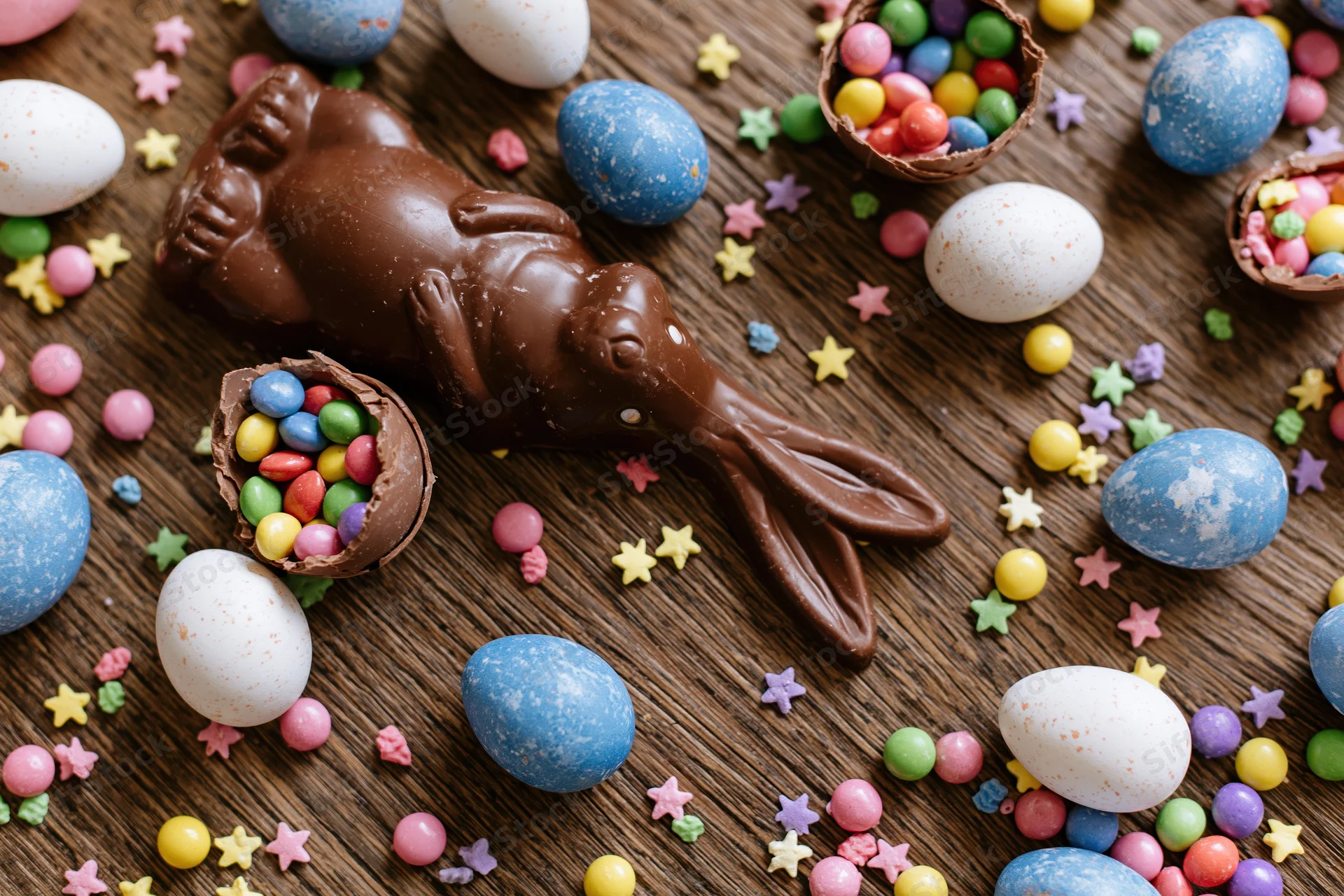 Chocolate easter bunny and colorful candy eggs arranged on dark wooden surface in flat lay overhead view