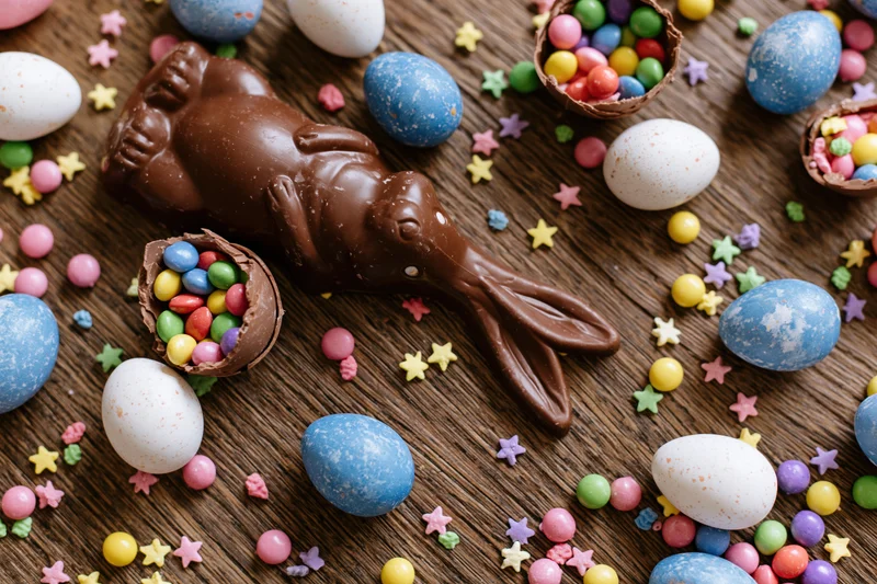 Chocolate easter bunny and colorful candy eggs arranged on dark wooden surface in flat lay overhead view