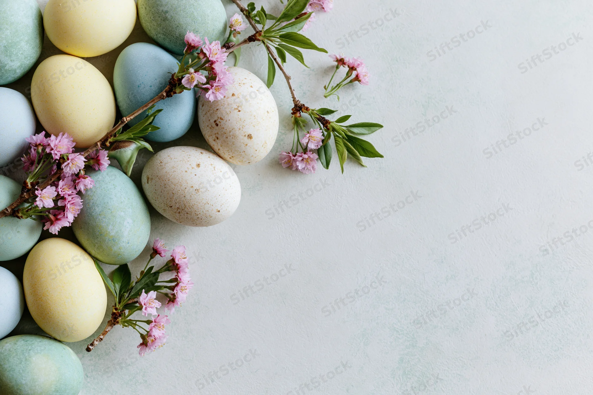 Pastel-dyed easter eggs and cherry blossom branches arranged on a white surface with copyspace