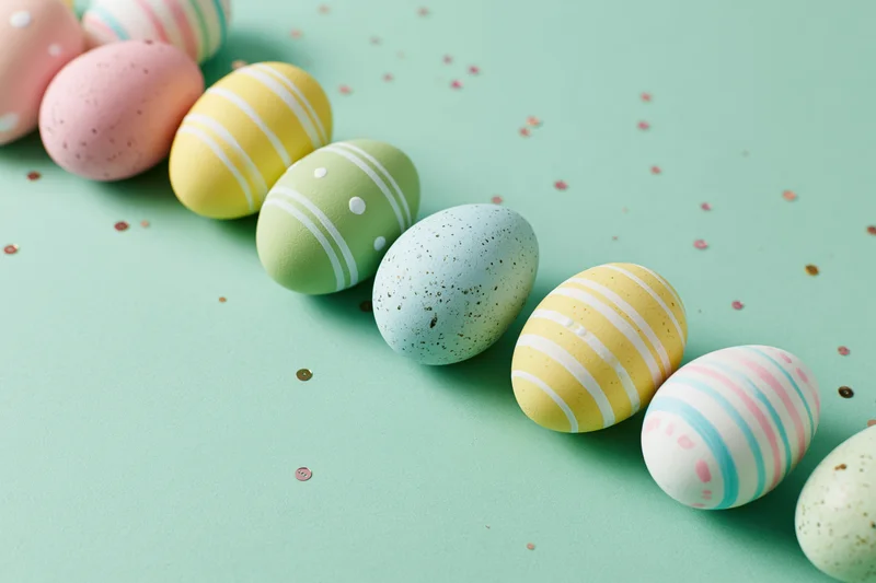 Pastel-painted easter eggs arranged in a loose diagonal row on a mint green surface with scattered confetti